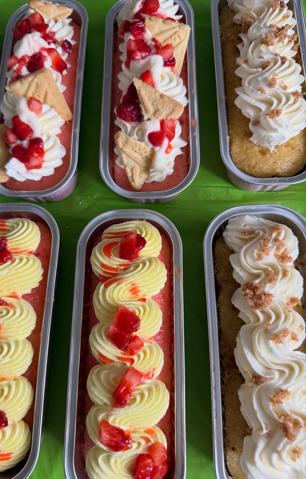 Mini loaf cakes in tins topped with cream, strawberries and cookie crumble